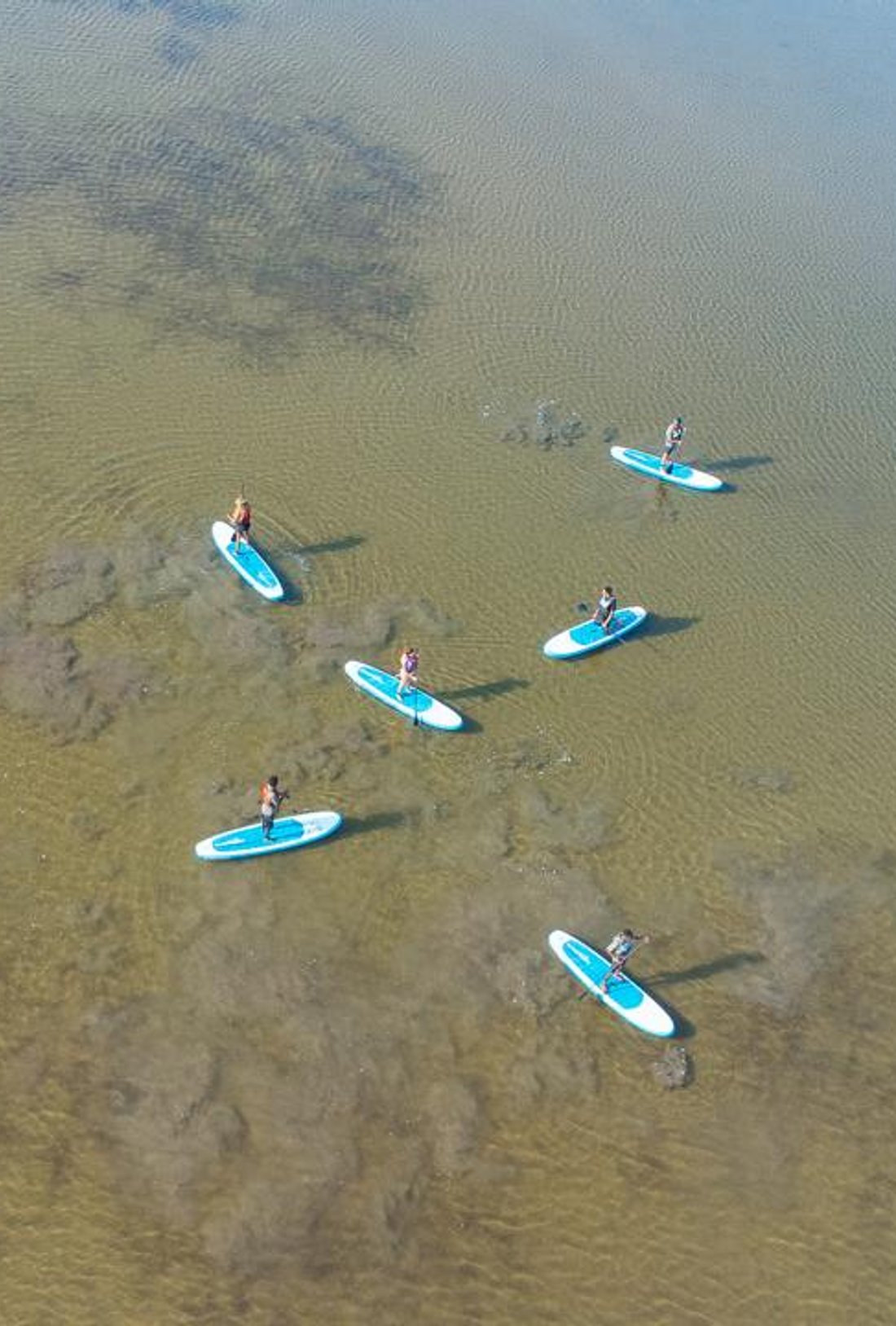 paddleboarders and kayakers in the creek in front of a village